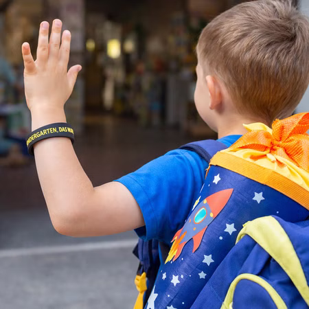 Silikon-Armband Kinder Kindergarten DAS WARS Abschied Geschenk Kita-Abschied ABC-Schütze Schulanfänger Endlich Schulkind Schulkind trägt schwarzes Silikon-Armband „Kindergarten DAS WARS“ beim Abschied aus dem Kindergarten mit Schulranzen.
