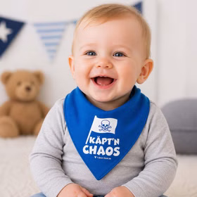 Lachendes Baby trägt ein blaues Piraten-Halstuch mit Aufdruck „Käpt’n Chaos“ und sitzt in einer hellen, freundlichen Umgebung.