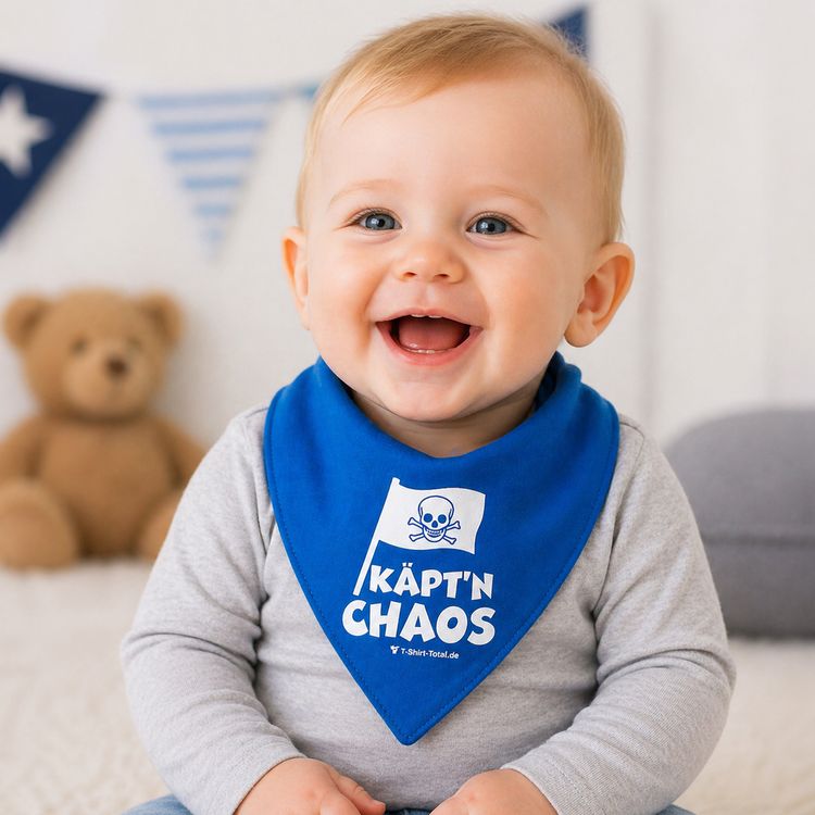 Lachendes Baby trägt ein blaues Piraten-Halstuch mit Aufdruck „Käpt’n Chaos“ und sitzt in einer hellen, freundlichen Umgebung.