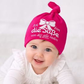 Baby Beanie Mütze Pink mit Spruch aus Baumwolle Neugeborene Mädchen Geschenk Geburt SALE Geschenkidee Neugeborenes Babyshower Pullerparty Lachendes Baby trägt pinke Beanie Mütze mit Spruch und Schleifenmotiv.