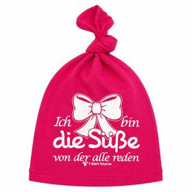 Lachendes Baby trägt pinke Beanie Mütze mit Spruch und Schleifenmotiv.