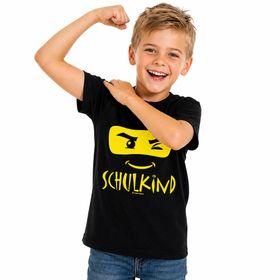 Fröhlicher Junge trägt schwarzes Schulkind T-Shirt mit Ninja-Motiv vorne und Wunschname „Jonas“ gelb auf dem Rücken.
