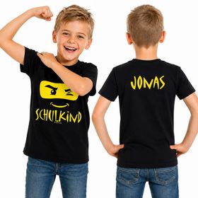 Fröhlicher Junge trägt schwarzes Schulkind T-Shirt mit Ninja-Motiv vorne und Wunschname „Jonas“ gelb auf dem Rücken.