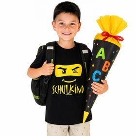 Fröhlicher Junge trägt schwarzes Schulkind T-Shirt mit Ninja-Motiv vorne und Wunschname „Jonas“ gelb auf dem Rücken.