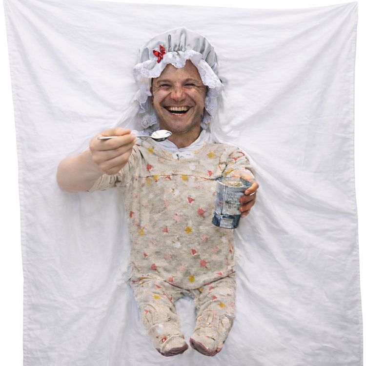 Bräutigam füttern Hochzeitsspiel für Erwachsene & für Geburtstag inkl. Anleitung Mann im Babykostüm lacht während eines Hochzeitsspiels, vor dekorierter Kulisse mit Lichtern und festlicher Atmosphäre.