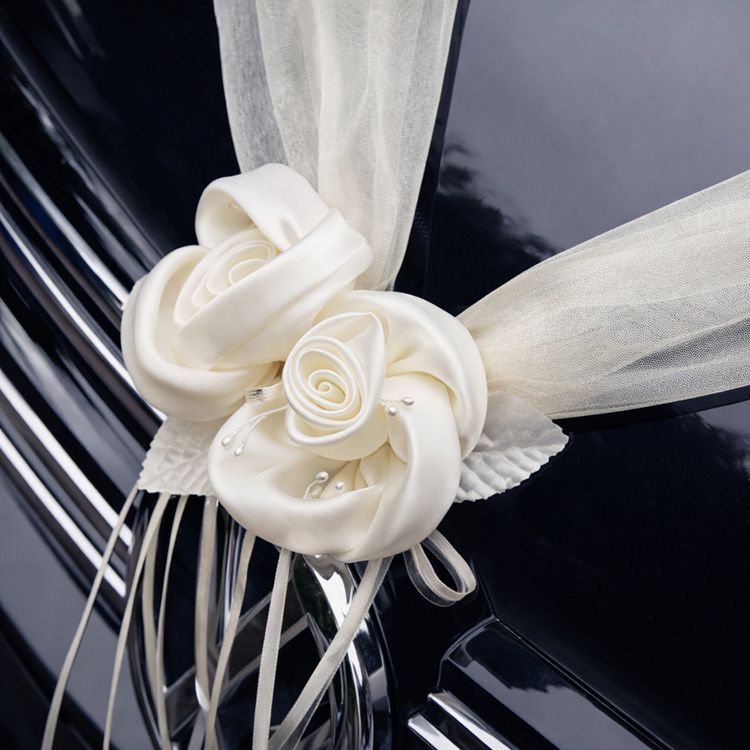 Cremefarbene Organza-Girlande mit Rosenblüten in V-Form auf der Motorhaube eines schwarzen Autos als elegante Hochzeitsdekoration befestigt.