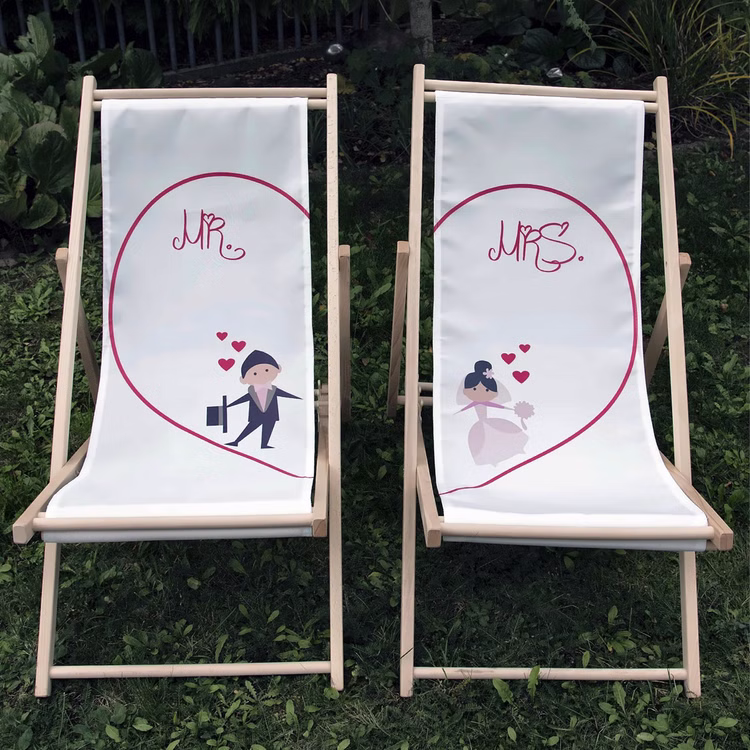 Hochzeits-Liegestuhl Mr. & Mrs. für Braut und Bräutigam Brautpaar individuelles Hochzeitsgeschenk 2 Liegestühle Geschenkidee zur Hochzeit Gastgeschenk Hochzeitsfeier Mr. & Mrs. Hochzeits-Liegestühle mit Classic Herz-Motiv nebeneinanderstehend auf grünem Rasen im Garten.
