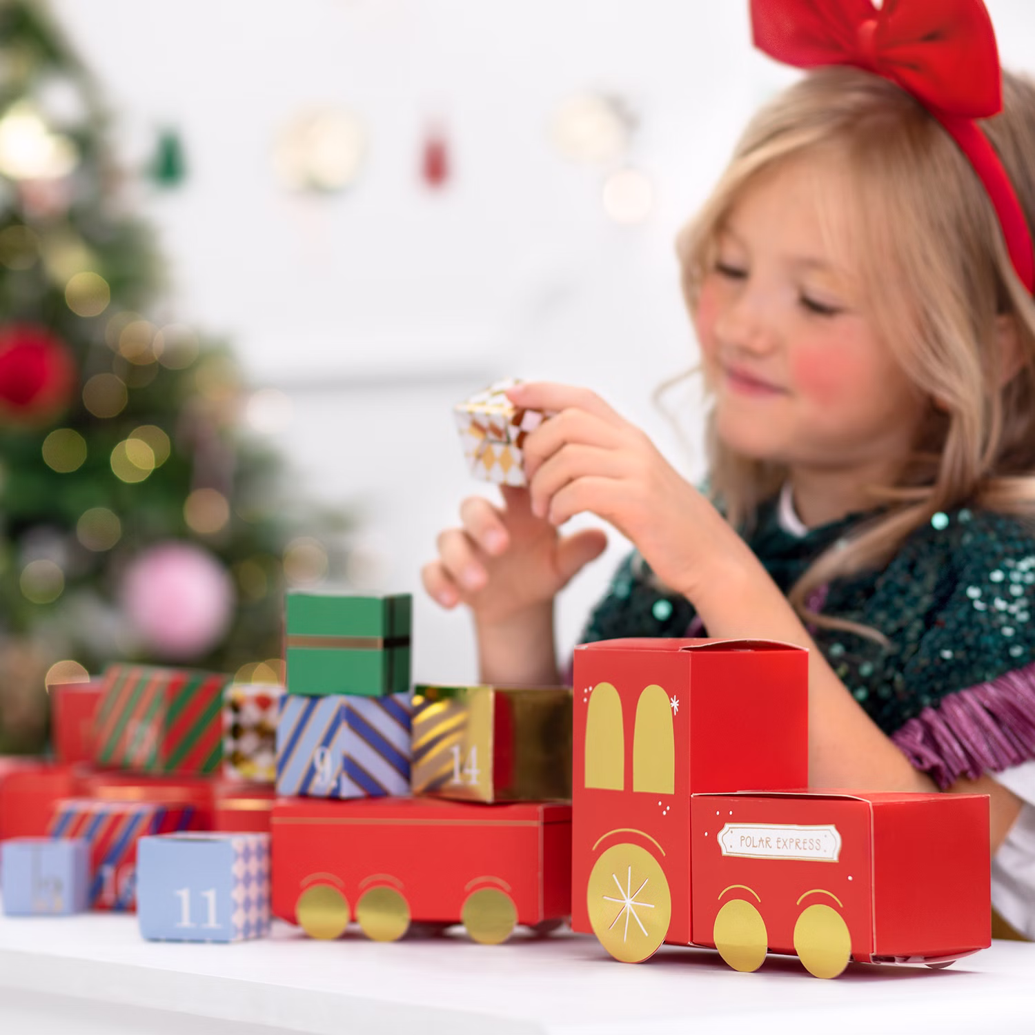 DIY Adventskalender Weihnachtszug zum Befüllen 24 Boxen aus Papier SALE 27-tlg. Bastel-Set 24 Schachteln, 50 cm Schnur, Brief an den Weihnachtsmann und Anleitung Geschenkidee Advent Adventszeit Kind spielt mit dem aufgebauten Adventskalender-Zug und öffnet eine der nummerierten Geschenkboxen.