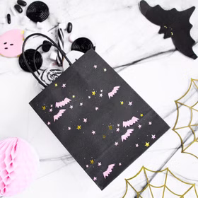 Halloween-Geschenktüte mit Fledermausmotiv gefüllt mit Süßigkeiten und Dekoration auf einem festlich dekorierten Tisch.
