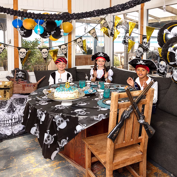 Piraten Geburtstag Kinder Mottoparty Dekoration Dekorierter Piraten-Kindergeburtstag mit verkleideten Gästen, Totenkopf-Tischdecke, Wimpelketten und passender Partydekoration.