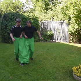 Wettrennen im Garten mit zwei Teams in grüner Doppelhose und orangefarbener Doppelhose