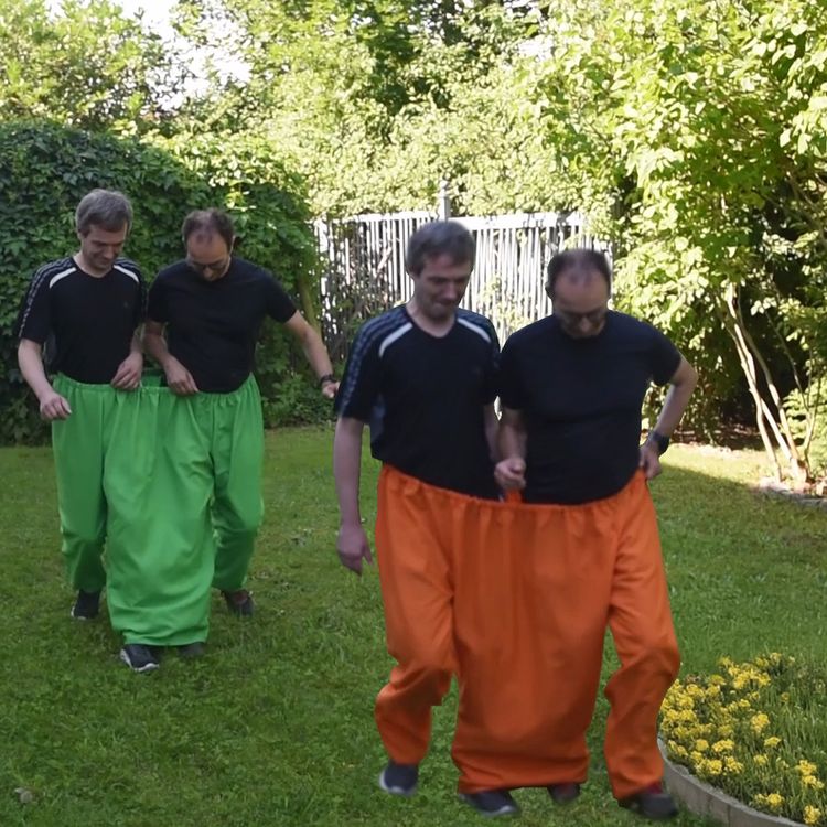 Wettrennen im Garten mit zwei Teams in grüner Doppelhose und orangefarbener Doppelhose