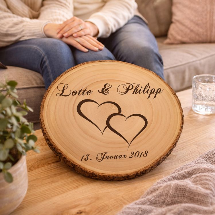 Personalisierte Baumscheibe mit Hochzeitsgravur als Dekoration auf einer festlich gedeckten Hochzeitstafel, im Hintergrund ein Brautpaar und Hochzeitsgäste in feierlicher Atmosphäre.