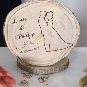Baumscheibe mit Gravur 30 cm Brautpaar Namen und Datum Hochzeit Jahrestag Geschenkidee Hochzeitsgeschenk Silberhochzeit Baumscheibe mit Gravur Lotte & Philipp 13. Januar 2018 mit Doppelherzen und Brautpaar-Motiv dekorativ in Szene gesetzt.
