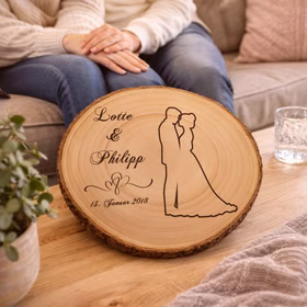 Baumscheibe mit Gravur 30 cm Brautpaar Namen und Datum Hochzeit Jahrestag Geschenkidee Hochzeitsgeschenk Silberhochzeit Gravierte Holzscheibe mit Hochzeitsmotiv liegt auf einem Couchtisch im Wohnzimmer, im Hintergrund sitzt ein Paar entspannt auf dem Sofa.