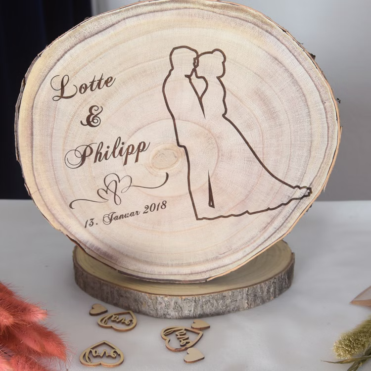 Baumscheibe mit Gravur 30 cm Brautpaar Namen und Datum Hochzeit Jahrestag Geschenkidee Hochzeitsgeschenk Silberhochzeit Baumscheibe mit Gravur Lotte & Philipp 13. Januar 2018 mit Doppelherzen und Brautpaar-Motiv dekorativ in Szene gesetzt.