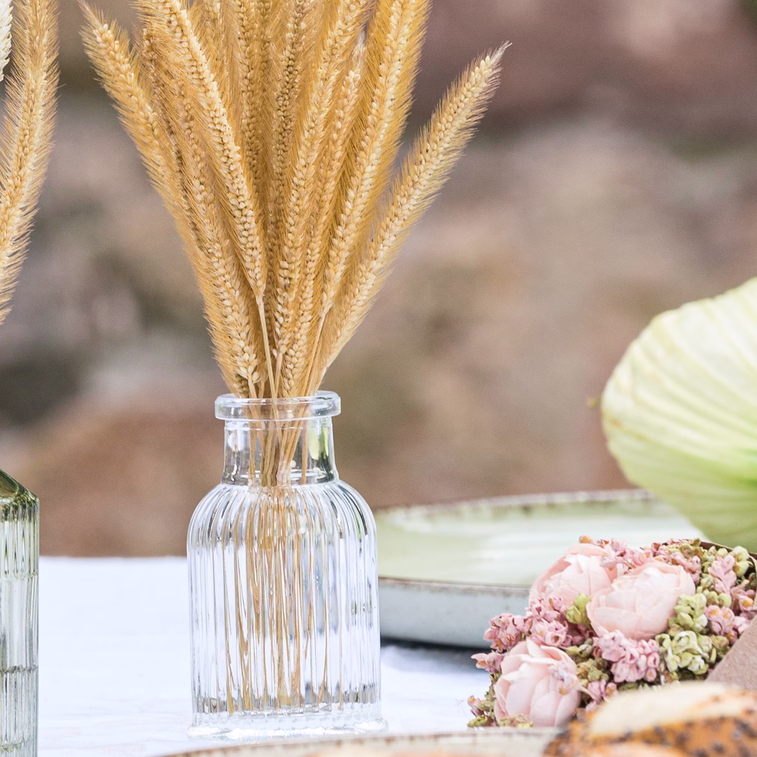 Transparente Deko-Vase mit Trockenblumen auf einem gedeckten Tisch dekoriert
