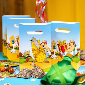 XXL Asterix & Obelix Geburtstag Party-Set Tisch-Deko 65-tlg. Part-Deko Kindergeburtstag Comic-Helden Dekoration gedeckter Tisch Hellblaue Geschenktüten mit Asterix- und Obelix-Motiven als dekorative Partyverpackung auf festlich gedecktem Tisch.