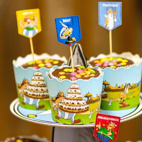 XXL Asterix & Obelix Geburtstag Party-Set Tisch-Deko 65-tlg. Part-Deko Kindergeburtstag Comic-Helden Dekoration gedeckter Tisch Detailaufnahme dekorierter Cupcakes in Asterix-Muffinformen mit Figurensteckern auf einem mehrstöckigen Präsentationsständer.