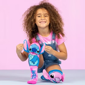 Kind sitzt lachend auf dem Boden und spielt mit den 3D-Ohren der Stitch-&-Angel-Socken, die farbenfroh in Pink und Blau gestaltet sind.