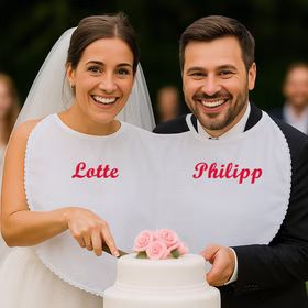 Braut & Bräutigam tragen das Doppel-Lätzchen mit Personalisierung und schneiden gemeinsam die Hochzeitstorte an