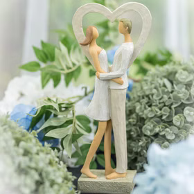 Figur eines Paares im Herzrahmen, aufgestellt zwischen grüner und blauer Blumendeko.