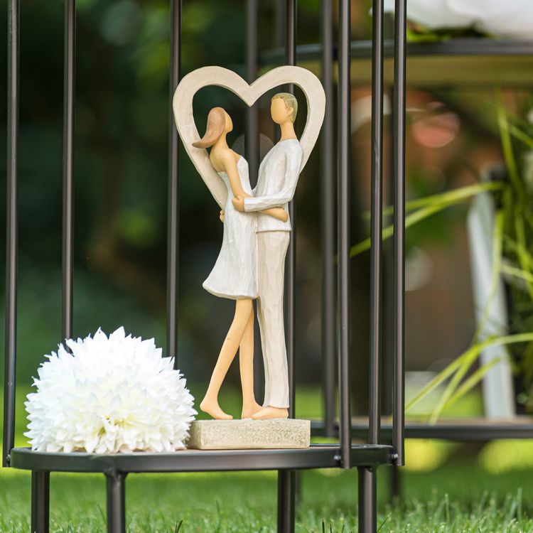 Figur eines Paares in Weiß im Herzrahmen, stehend und umarmend, auf rechteckigem Sockel.