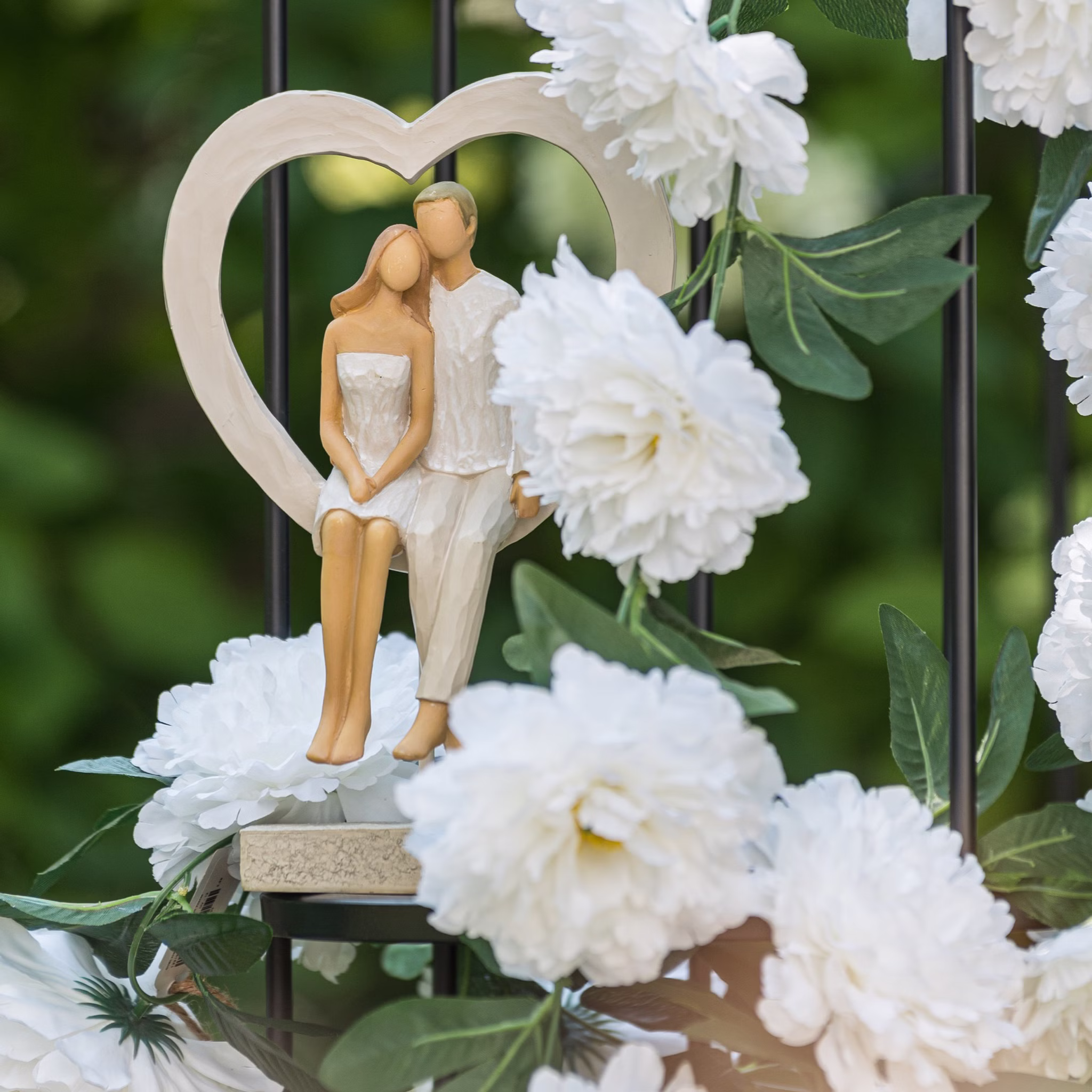Brautpaar Figur Sitzend Liebe Weiß mit Herz Tischdeko Hochzeits-Deko Tisch-Deko Deko-Ideen Geschenkidee Braut & Bräutigam Brautpaar-Figur im Herzrahmen, dekoriert zwischen weißen Blumen im Garten.