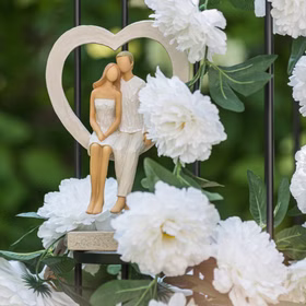 Brautpaar-Figur im Herzrahmen, dekoriert zwischen weißen Blumen im Garten.