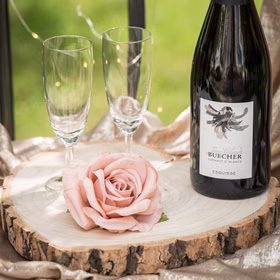 Baumscheibe Herzform Rustikales Holzherz 23 cm Tischdeko Hochzeit Geburtstag Vintage Dekoration Geburtstag Hochzeit Jubiläum Muttertag Deko-Ideen Dekorierte Holzscheibe mit Sektflasche, Gläsern und rosa Rose.