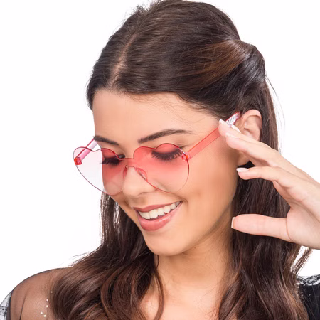 Herzbrille Rosa Taylor 14 x 14 cm 80er Party Kostüm-Zubehör für Damen Kostüm-Zubehör Sommer-Party Festival 80er 90er Mottoparty Fasching Karneval Frau mit rosa Herz-Sonnenbrille, Blick nach unten und Lächeln.