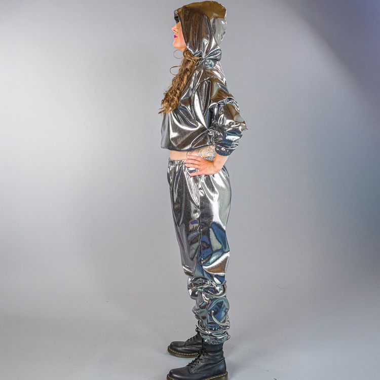 Mann und Frau tragen silberne Jogginganzüge mit Kapuze, er steht mit pinker Cap und Getränk, sie hockt mit auffälligem Make-up.