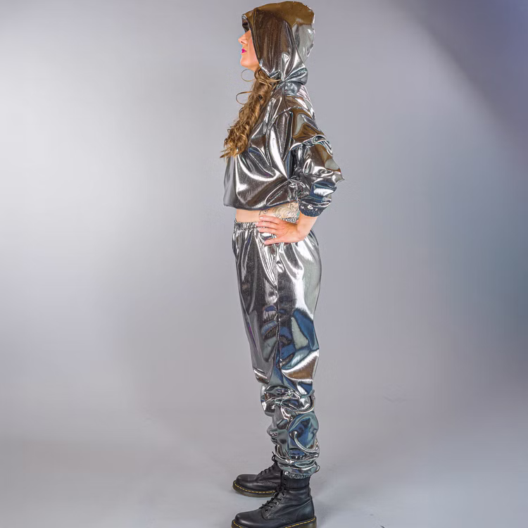 90er Jahre Space Kostüm Silver Flash Rave für Erwachsene Gr. M-XL Paarkostüm Gruppenkostüm Fasching Karneval 80er und 90er Mottoparty Seitenansicht der Frau im silbernen Jogginganzug mit Kapuze, Hände in die Hüften gestützt.