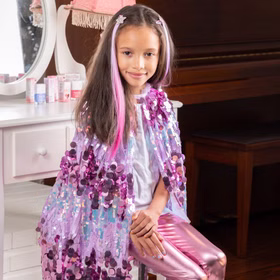 Bunte Haarsträhnen mit Clip 8 Stück Pink & Lila Prinzessin Fee Extensions für Kinder Geschenkidee Geburtstag Fasching Karneval Rollenspiel Verkleidung Kind sitzt am Schminktisch mit glitzerndem Cape und trägt pinke Haarsträhnen mit Sternclips.
