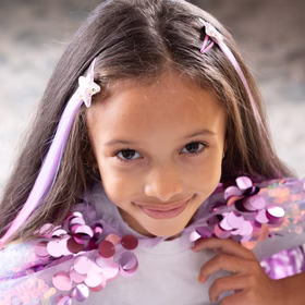 Bunte Haarsträhnen mit Clip 8 Stück Pink & Lila Prinzessin Fee Extensions für Kinder Geschenkidee Geburtstag Fasching Karneval Rollenspiel Verkleidung Mädchen mit lila-pinken Haarsträhnen im Haar, trägt glitzerndes Cape und schaut lächelnd in die Kamera.