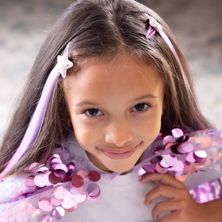 Bunte Haarsträhnen mit Clip 8 Stück Pink & Lila Prinzessin Fee Extensions für Kinder Geschenkidee Geburtstag Fasching Karneval Rollenspiel Verkleidung Mädchen mit lila-pinken Haarsträhnen im Haar, trägt glitzerndes Cape und schaut lächelnd in die Kamera.