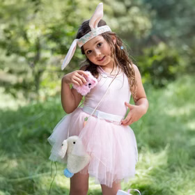 Mädchen mit rosa Tutu-Kleid und Hasenohren-Stirnband posiert auf einer Wiese, trägt die Plüsch-Hasentasche umgehängt und hält ein kleines pinkes Plüschtier.