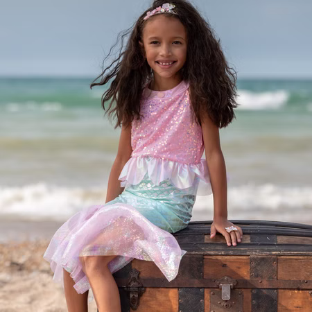 Meerjungfrauen Kostüm Mermaid Sirena Glitzerflosse für Kinder 3-8 Jahre Rosa Nixe Mermaid Kostüm Fasching Karneval Mottoparty Kindergeburtstag Mädchen trägt Meerjungfrauenkostüm und sitzt lächelnd auf einer alten Schatztruhe am Strand mit Meer im Hintergrund.