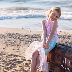 Meerjungfrauen Kostüm Mermaid Sirena Glitzerflosse für Kinder 3-8 Jahre Rosa Nixe Mermaid Kostüm Fasching Karneval Mottoparty Kindergeburtstag Mädchen sitzt am Strand in Meerjungfrauenverkleidung auf einer Schatztruhe, bunte Perlenketten hängen heraus.