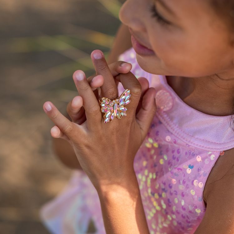 Mädchen trägt Meerjungfrauenkostüm und sitzt lächelnd auf einer alten Schatztruhe am Strand mit Meer im Hintergrund.