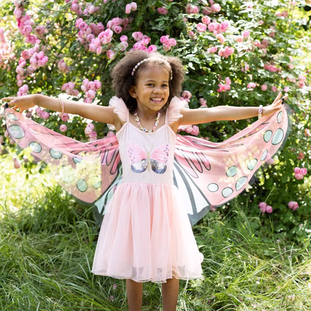 Schmetterling Kostüm Fee Rosalie Kleid mit Flügeln für Kinder 5-6 Jahre Tierkostüm Fasching Karneval Mottoparty Kindergeburtstag Ein Mädchen im Schmetterlingskleid breitet die rosa Flügel im Garten vor einer Rosenhecke weit aus.