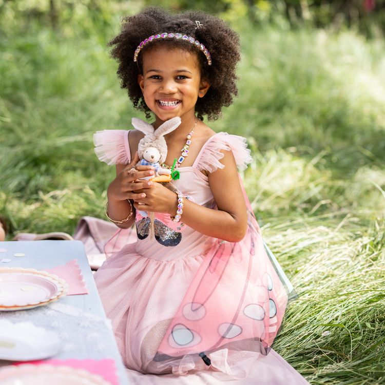 Schmetterling Kostüm Fee Rosalie Kleid mit Flügeln für Kinder Ein Mädchen im Schmetterlingskleid breitet die rosa Flügel im Garten vor einer Rosenhecke weit aus.