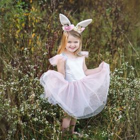 Mädchen im Osterhase Flocke Kostüm hebt spielerisch den rosa Tüllrock an, während es in einer Wiese steht.