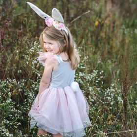 Mädchen im Osterhase Flocke Kostüm hebt spielerisch den rosa Tüllrock an, während es in einer Wiese steht.