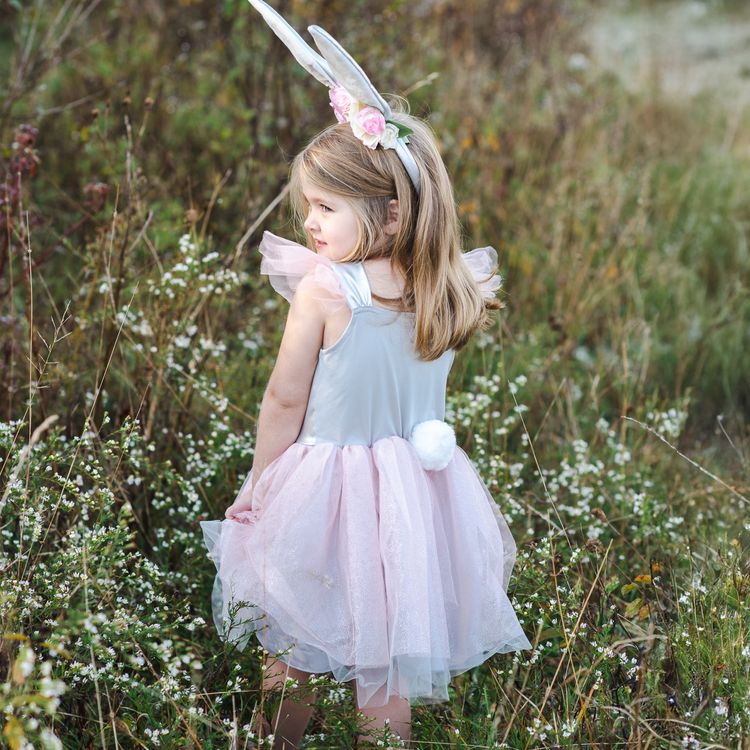 Mädchen im Osterhase Flocke Kostüm hebt spielerisch den rosa Tüllrock an, während es in einer Wiese steht.