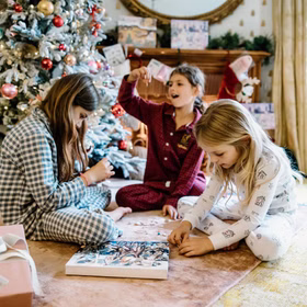 Drei Kinder in Pyjamas sitzen vor dem Weihnachtsbaum und basteln mit Charms aus dem Adventskalender.