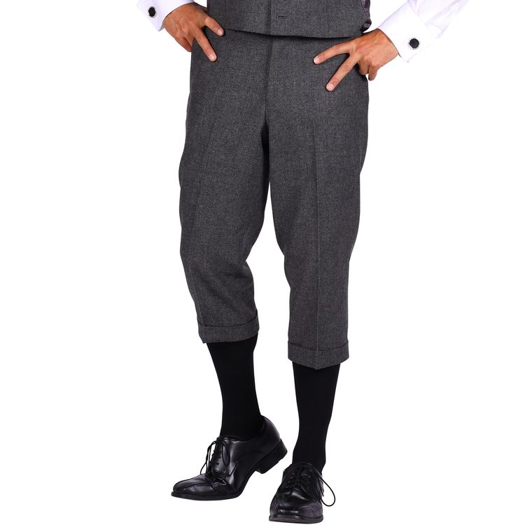 Ein Mann trägt ein komplettes Kostüm im 20er-Jahre-Stil mit grauer Weste, Knickerbockerhose, weißem Hemd, schwarzer Krawatte und schwarzen Schuhen.
