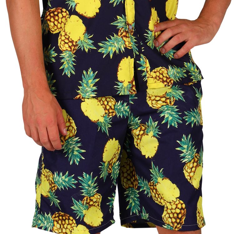 Ein Mann trägt ein sommerliches Outfit mit kurzer Ananas-Hose und passendem Hemd in Schwarz mit gelbem Ananasmuster.
