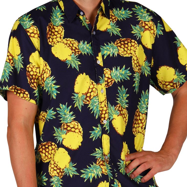Ein Mann trägt ein sommerliches Outfit mit kurzer Ananas-Hose und passendem Hemd in Schwarz mit gelbem Ananasmuster.