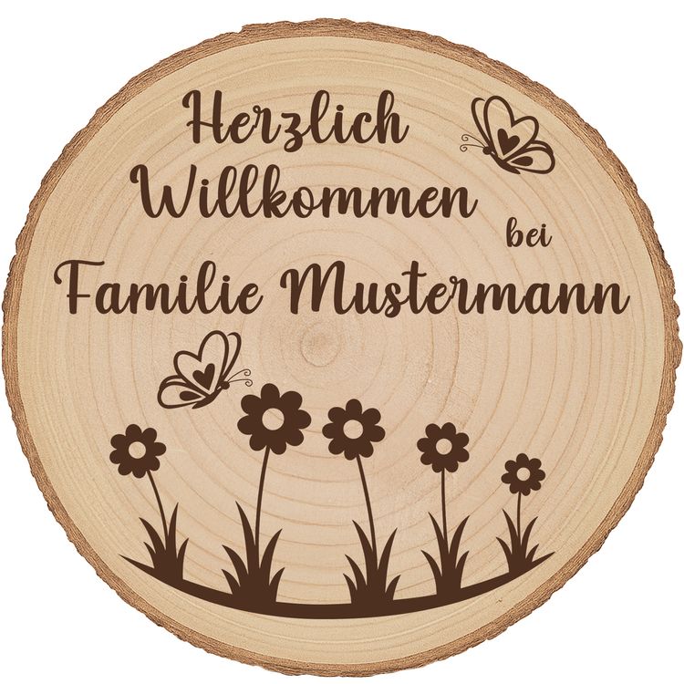 Personalisierte Baumscheibe mit Rinde und Gravur „Herzlich Willkommen bei Familie Schmidt“, dekoriert mit Schmetterlingen und Blumenmotiv, platziert in einem farbenfrohen Sommer-Blumenbeet am Hauseingang.